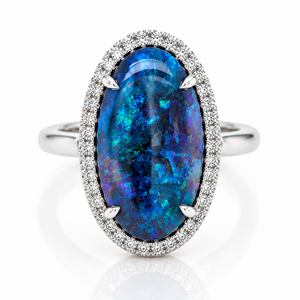 An oval-cut blue opal ring set in a silver-toned halo with small pavé diamonds, shown on a clean white background with a soft reflection below.
