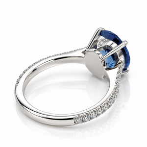 A silver-tone ring featuring a large oval blue gemstone in a prong setting, with a pavé band accented by small clear stones, shown on a white background.